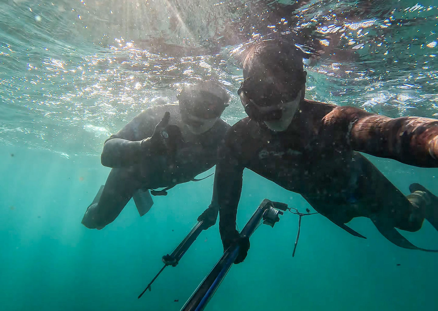 Two spearfishermen at the surface, one giving a thumbs-up to his buddy